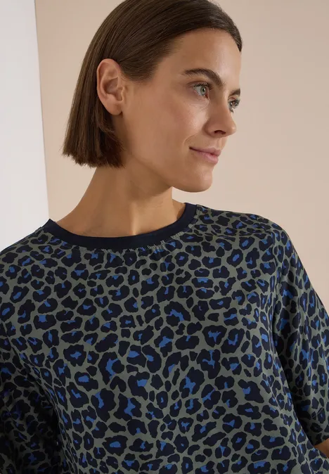 Blouse met korte mouwen en luipaardprint dried olive green Nahaufnahme einer Frau im blau-schwarzen Leo-Pullover mit schulterlangem Haar.