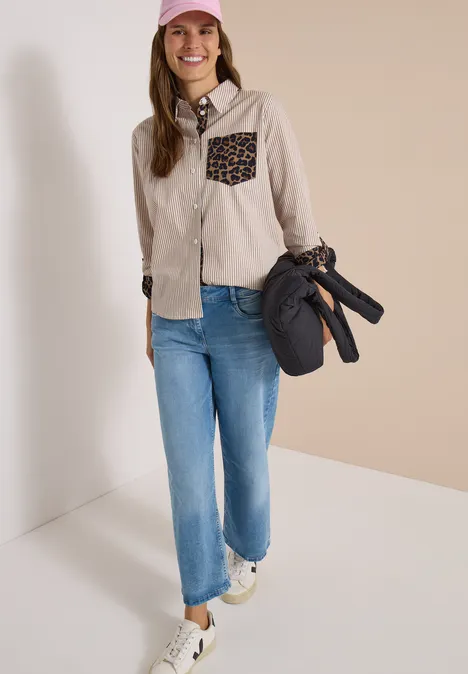 Hemdbluse mit Streifen und Leo-Brusttasche creamy mocha Frau in Jeans, heller Jacke mit Leoparden-Tasche, Cap und Sneakern, trägt eine Tasche mit Stativ.