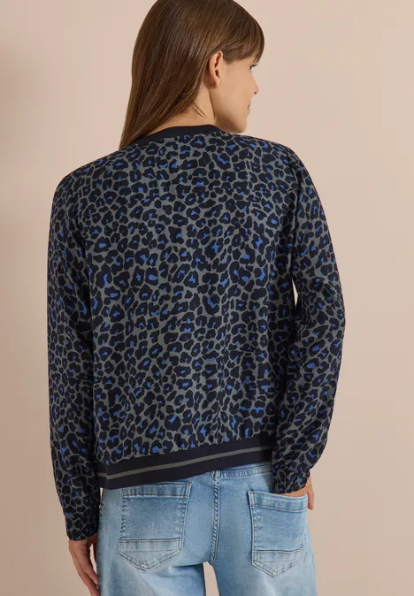 Femme vue de dos portant un pull léopard bleu et noir avec un jean bleu clair.