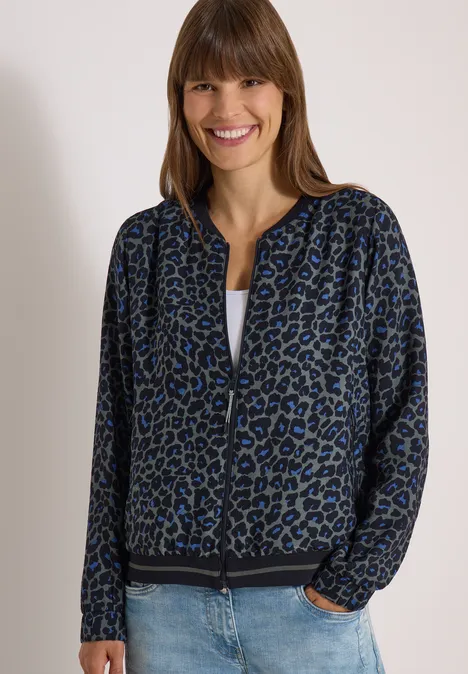 Femme souriante en veste léopard bleue, tee-shirt blanc et jean.