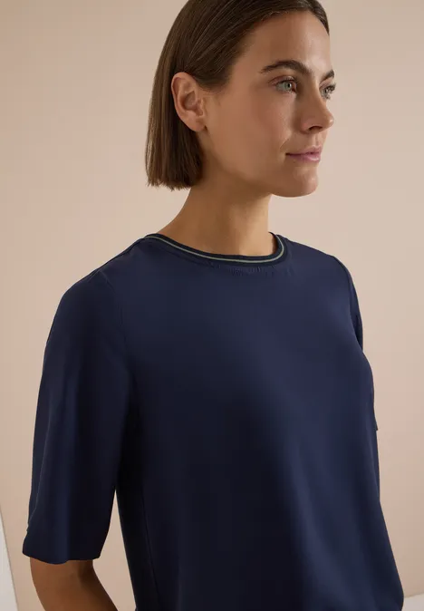 Blouse met korte mouwen en ronde hals urban dark blue Eine Frau in Seitenansicht trägt ein dunkelblaues, kurzärmeliges Oberteil mit mehrfarbigem Kragen.