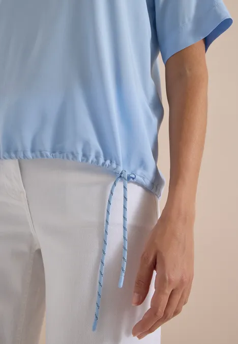 Nahaufnahme eines hellblauen Oberteils mit Kordelzug und einer weißen Hose.