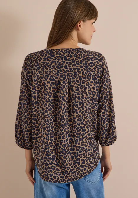 Tuniek met 3/4-mouwen, split in de hals en luipaardprint creamy mocha Vrouw van achteren in losvallende, bruin-zwarte luipaardblouse en blauwe jeans voor een neutrale achtergrond.