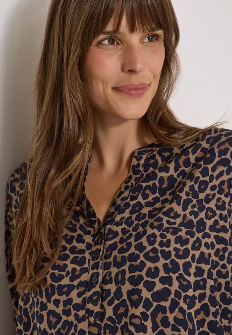 Tuniek met 3/4-mouwen, split in de hals en luipaardprint creamy mocha Vrouw in bruin-zwarte luipaardblouse, schouderlang haar, glimlachend en opzij kijkend.