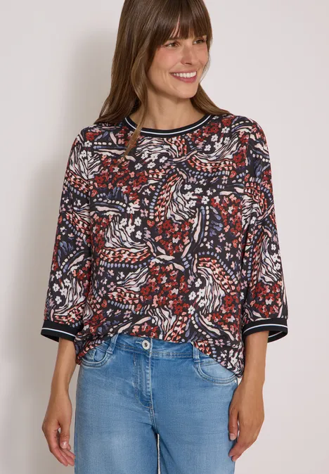 Blouse met 3/4-mouwen en print raw chocolate brown Vrouw in kleurrijke blouse met print en spijkerbroek lacht voor lichte achtergrond.