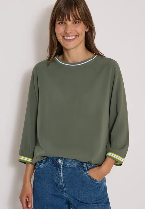Blouse met 3/4-mouwen en contrasterende details dried olive green Vrouw lacht in een comfortabel olijfgroen sweatshirt met streepdetails, driekwartmouwen en jeans.