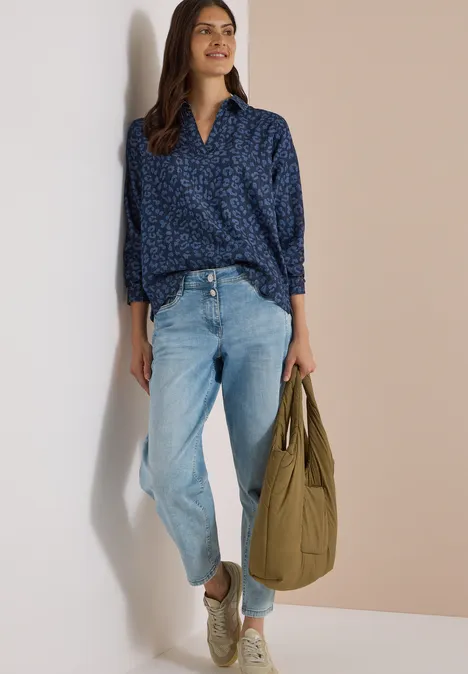 Langarm Bluse mit Laser-Print Dark blue wash Frau lehnt lässig an einer Wand, trägt eine blaue Bluse, helle Jeans und weiße Sneaker, hält eine grüne Tasche.