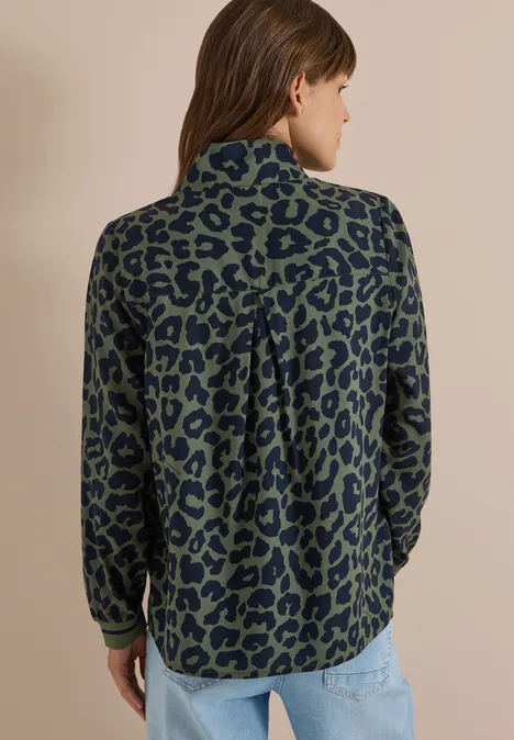 Frau von hinten in blau-grüner Bluse mit schwarzem Leopardenmuster und Jeans