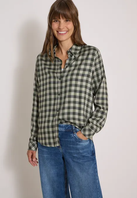 Chemisier à manches longues à carreaux khaki Femme portant une chemise verte à carreaux et un jean bleu, souriante, main droite dans la poche.