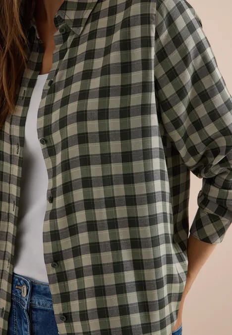 Chemisier à manches longues à carreaux khaki Femme en chemise à carreaux vert et beige sur débardeur blanc et jean.