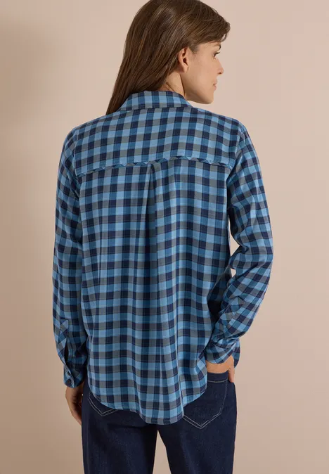 Eine Person von hinten in einem blauen, karierten Hemd vor beigem Hintergrund.
