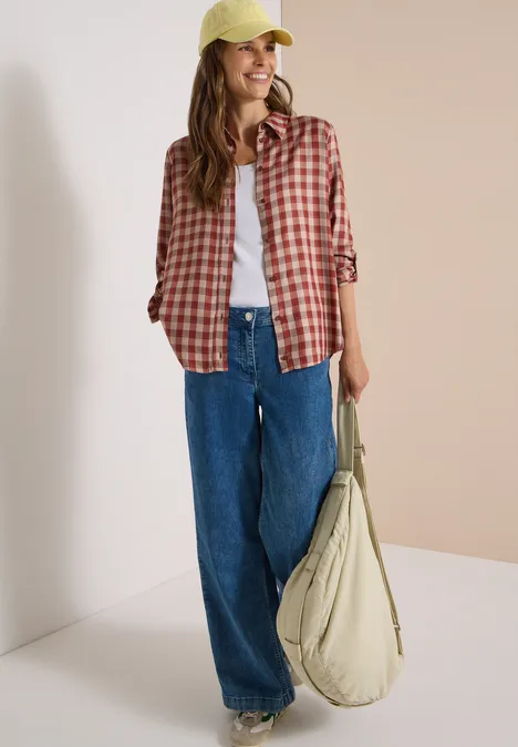 Chemisier à manches longues à carreaux dark russet red Jeune femme en jean large, t-shirt blanc, chemise à carreaux rouge, casquette jaune et sac vert.