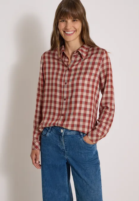 Chemisier à manches longues à carreaux dark russet red Femme souriante portant une chemise à carreaux et un jean devant un fond neutre.