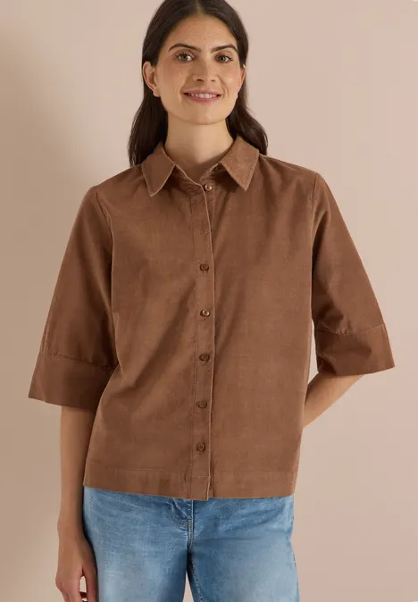 Overhemd met korte mouwen in effen kleur creamy mocha Een vrouw draagt een bruine corduroy blouse met 3/4-mouwen, kraag en knopen, lichtblauwe jeans op een beige achtergrond.
