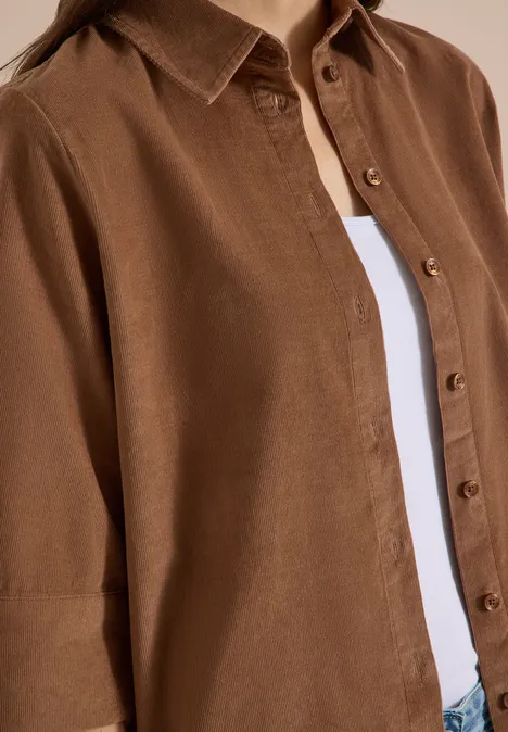Overhemd met korte mouwen in effen kleur creamy mocha Bruin linnen overhemd met knopen over een wit T-shirt, close-up van het bovenlijf.