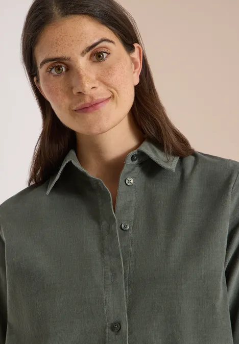 Overhemd met korte mouwen in effen kleur dried olive green Portret van een glimlachende vrouw met donker haar in een groene blouse tegen neutrale achtergrond.