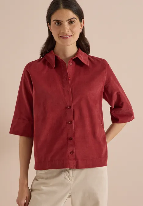 Overhemd met korte mouwen in effen kleur russet red Vrouw draagt rode corduroy blouse met driekwartmouwen en beige broek tegen lichte achtergrond.