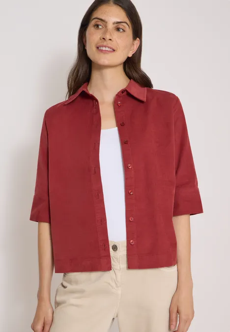 Overhemd met korte mouwen in effen kleur russet red Vrouw in bordeauxrood overhemd met driekwart mouwen, wit topje en lichte broek voor neutrale achtergrond.