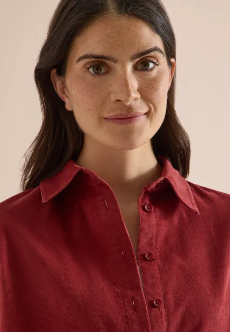 Overhemd met korte mouwen in effen kleur russet red Vrouw met donker haar en sproeten in een rood overhemd, vriendelijk glimlachend naar de camera.