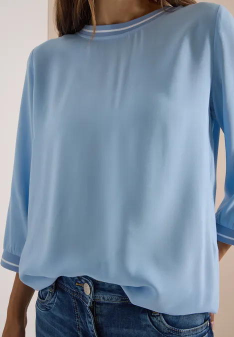 Person trägt hellblaue, lockere Bluse mit 3/4-Ärmeln und Jeans.