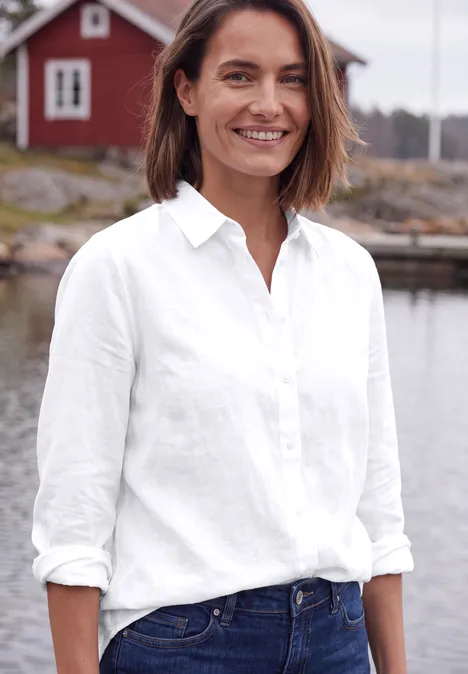 Langarm Hemdbluse mit Knopfleiste White Lächelnde Frau in weißer Bluse und Jeans vor einem See mit rotem Haus im Hintergrund.
