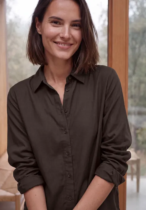 Eine lächelnde Frau in brauner Bluse vor hellem Hintergrund.