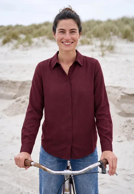 Chemisier à manches longues avec patte de boutonnage red wine Eine lächelnde Frau mit rotem Hemd und Jeans steht am Strand und hält ihr Fahrrad.