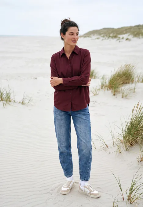 Chemisier à manches longues avec patte de boutonnage red wine Frau in Jeans und Hemd steht lächelnd barfuß auf einem Dünenstrand mit Gras im Hintergrund.