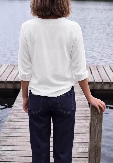 Langarm Tunika mit Split Neck White Rückansicht einer Frau mit weißem Oberteil und Jeans auf einem Holzsteg am Wasser