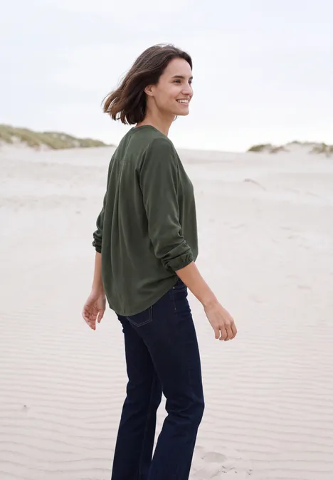 Een vrouw in groene trui en spijkerbroek wandelt over het strand.