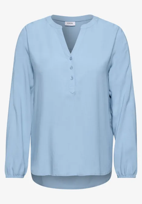 Lichtblauwe blouse met lange mouwen, V-hals zonder kraag en knoopsluiting.
