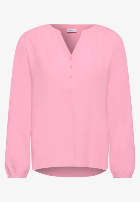 Lichte roze blouse met V-hals en halve knoopsluiting, lange mouwen en losse pasvorm.