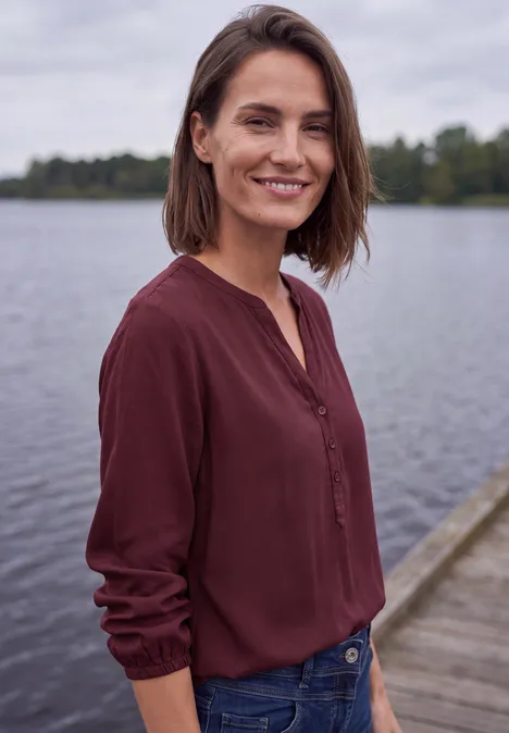 Een glimlachende vrouw staat op een steiger voor rustig water.