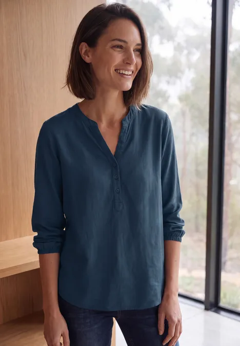 Langarm Tunika mit Split Neck moonlight blue Eine lächelnde Frau in blauer Bluse vor einem Fenster.