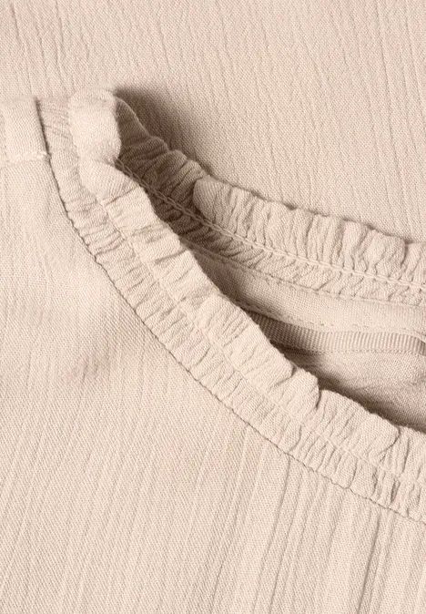 Gros plan d’un haut beige clair avec un col à volants froncés.