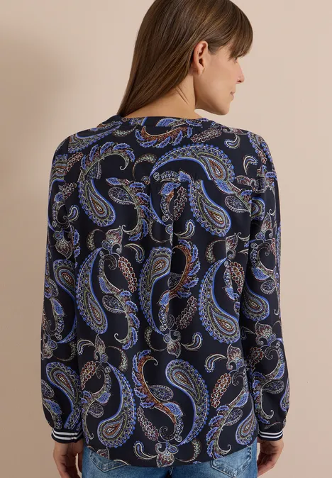 Frau von hinten in dunkelblauer Bluse mit blauem Paisley-Muster, seitliche Ansicht, schulterlanges Haar
