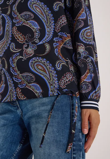 Dunkle Bluse mit buntem Paisley-Muster, kombiniert mit Jeans.