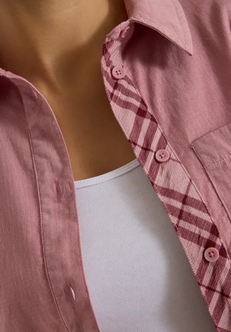 Eine Nahaufnahme einer Person, die ein rosa Hemd über einem weißen Tanktop trägt.