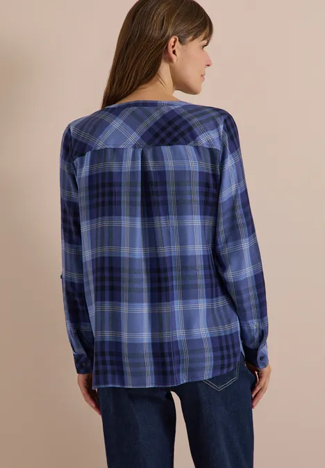 Frau von hinten in blau kariertem Hemd mit Jeans vor beigem Hintergrund.