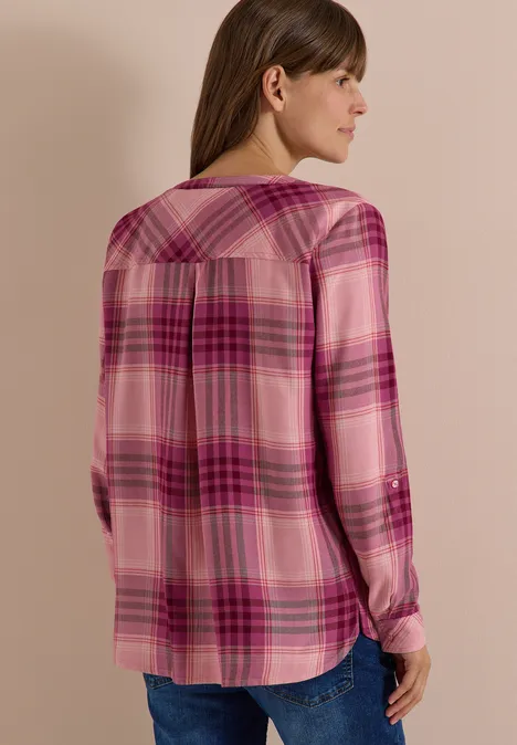 Frau von hinten in pink-kariertem Langarmhemd und blauer Jeans vor neutralem Hintergrund.