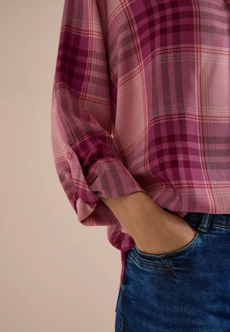 Eine Person trägt eine rosa-karierte Bluse mit hochgekrempelten Ärmeln und Jeans.