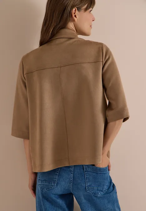 Rückenansicht einer Frau in beige-brauner, kastiger Jacke mit Dreiviertelärmeln und Jeans.