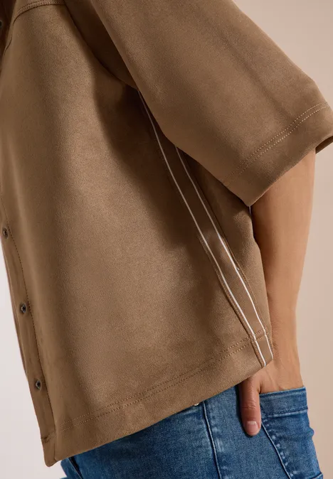Braunes Oberteil mit Knöpfen und weißen Paspeln, Hand in der Jeans-Tasche