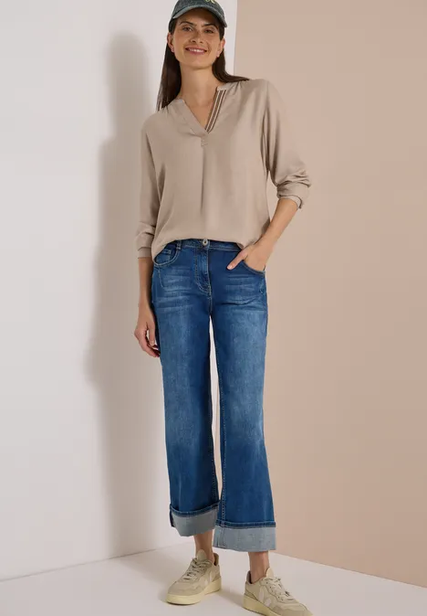 Langarm Tunika mit Split Neck und Tape creamy mocha melange Frau vor neutralem Hintergrund in beigefarbener Bluse, umgeschlagener Jeans, Sneakern und Baseballcap.
