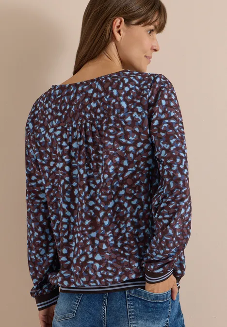 Vrouw van achteren in blauw-bruin gebloemde blouse met lange mouwen en gestreepte boorden.