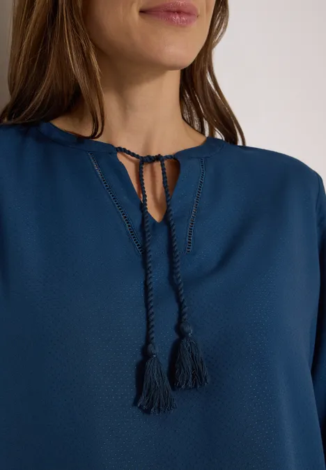 Frau in blauer Bluse mit V-Ausschnitt, Kordelzug und Quasten-Detail.