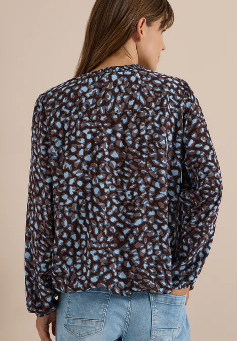 Vrouw van achteren in donkerbruine blouse met lichtblauwe luipaardprint en lichte spijkerbroek.