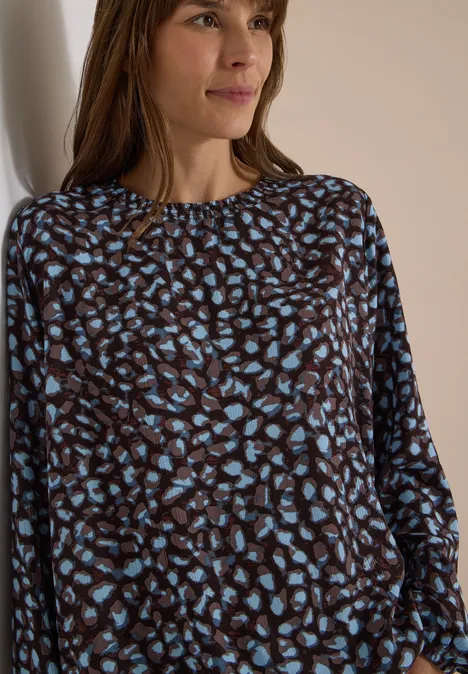 Vrouw met een bruin-blauw gemêleerde top voor een neutrale achtergrond.
