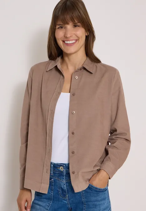 Chemisier à manches longues en velours côtelé earthy taupe Une femme souriante porte une veste marron sur un débardeur blanc et un jean.
