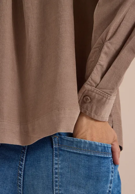 Chemisier à manches longues en velours côtelé earthy taupe Gros plan d’une main glissée dans une poche de jean bleu sous une chemise beige.